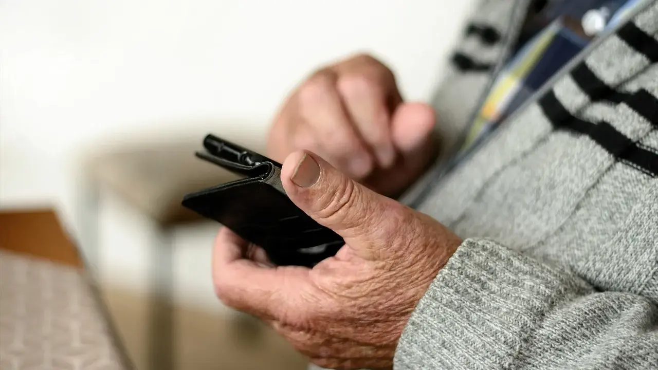 Mani anziane che tengono uno smartphone, forse per capire come fare lo SPID.