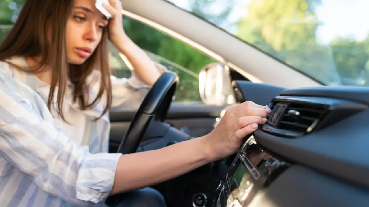 Donna in auto, con un fazzoletto sulla fronte, soffre di sudorazione eccessiva al minimo sforzo, cercando sollievo vicino alla bocchetta dell'aria.