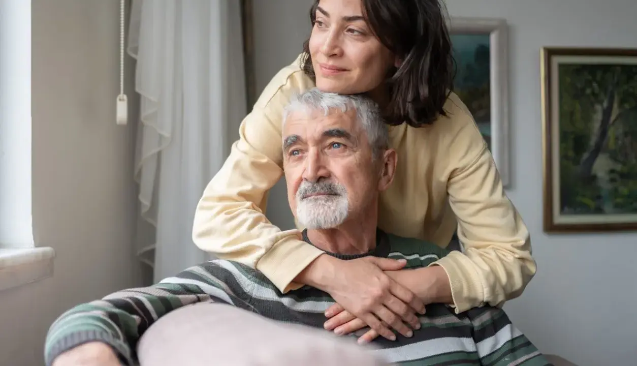 Un uomo anziano con Alzheimer, abbracciato da una donna, sembra cogliere un momento di lucidità, un ricordo che riaffiora.