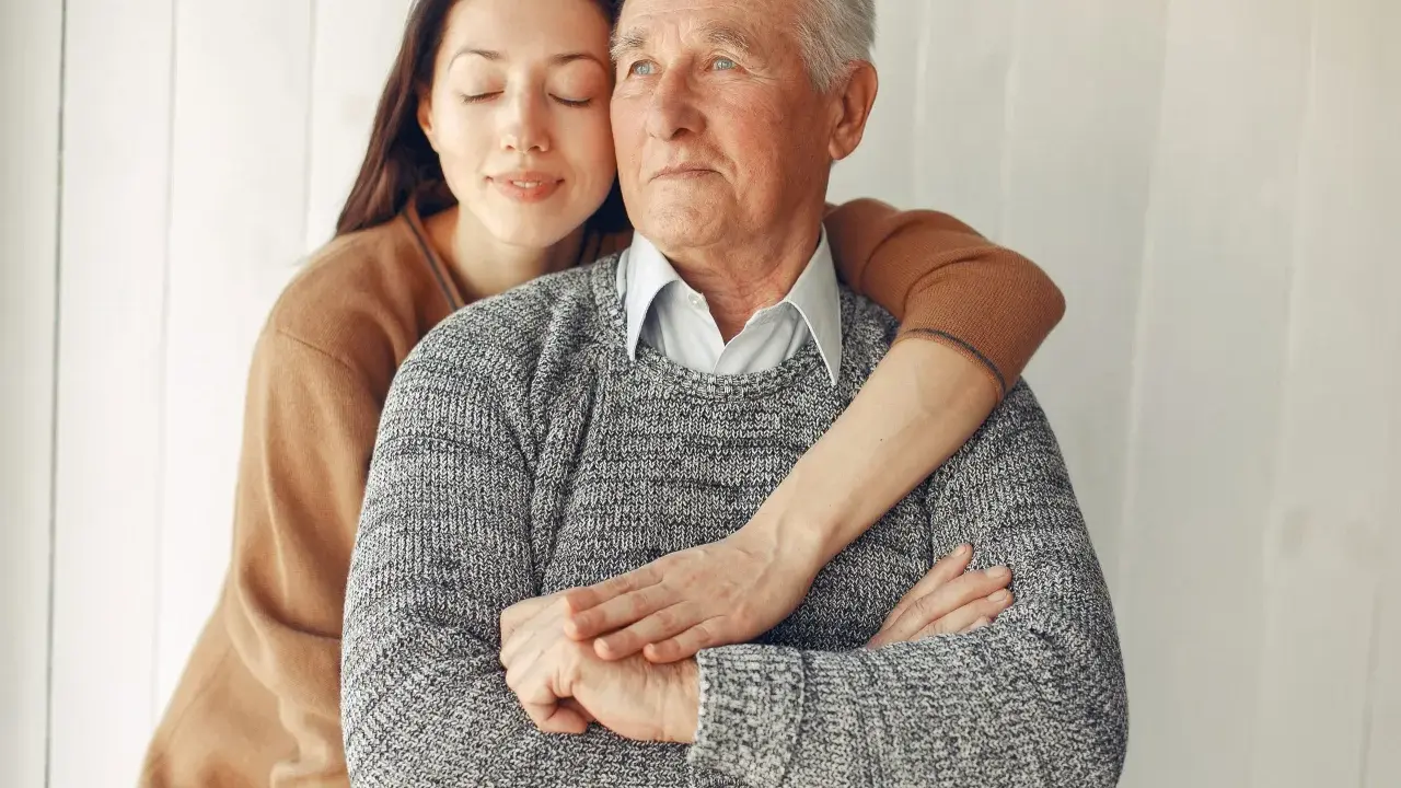Un abbraccio affettuoso: un modo per come calmare una persona con demenza senile. La giovane donna stringe dolcemente l'anziano uomo, offrendo conforto e sicurezza.