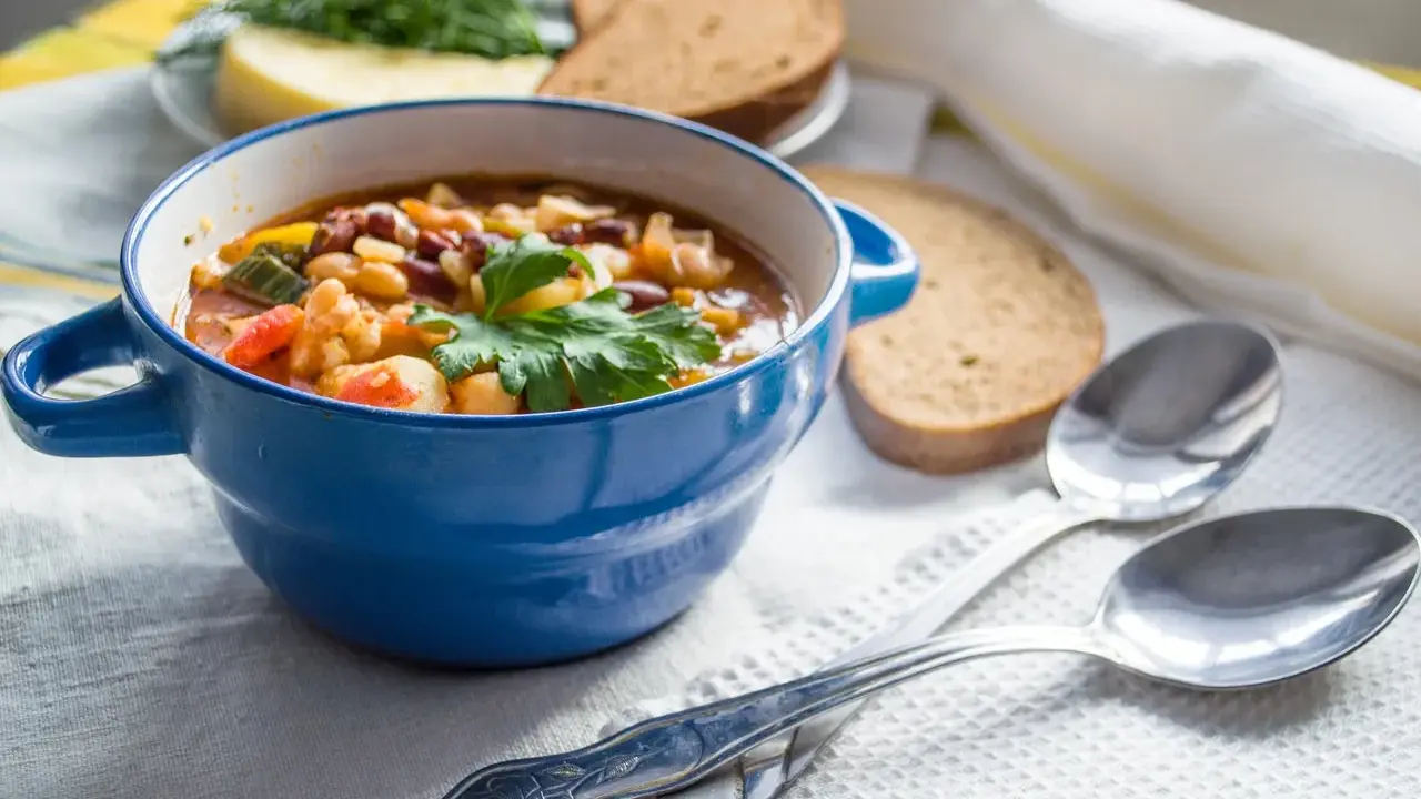 Zuppa nutriente, ideale per una dieta per anziani over 90. Servita in ciotola blu con pane integrale e erbe fresche.