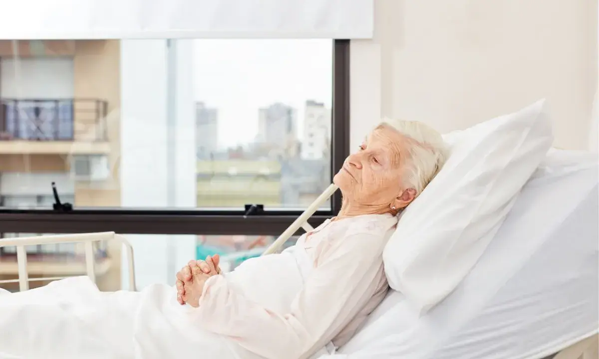 Anziana allettata in ospedale, con mani giunte. La domanda "quanto può vivere un anziano allettato" è complessa e dipende da molti fattori.