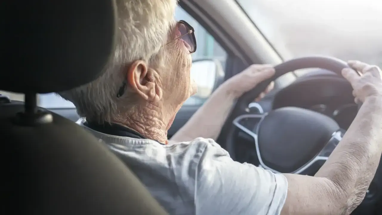 Anziana al volante, con mani sul volante, potrebbe suggerire il tema del decadimento cognitivo nell'anziano e la sua autonomia.