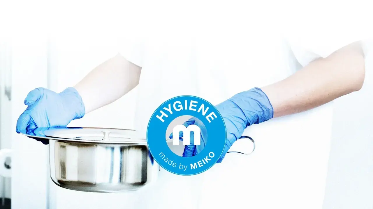 Mani guantate presentano una padella metallica, pronta per essere usata. Il logo MEIKO sottolinea l'igiene.
