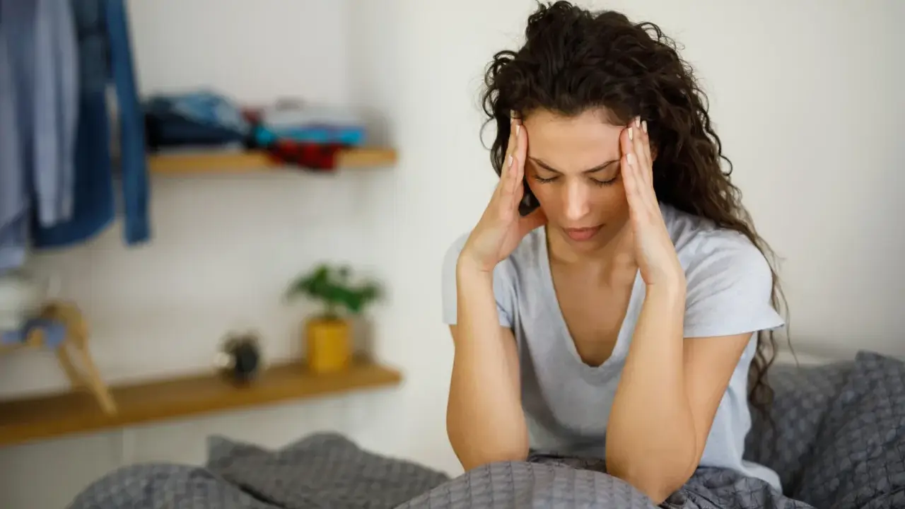 Donna con le mani sulle tempie, seduta a letto, soffre di giramenti di testa.