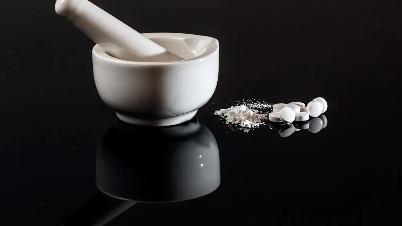Mortaio e pestello con polvere bianca e pillole, forse per una preparazione farmaceutica con esenzione 013.