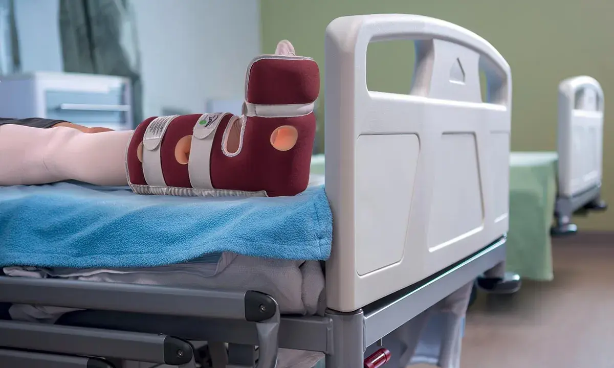 Piede con tutore per prevenire la piaga da decubito sul tallone, appoggiato su un letto ospedaliero.