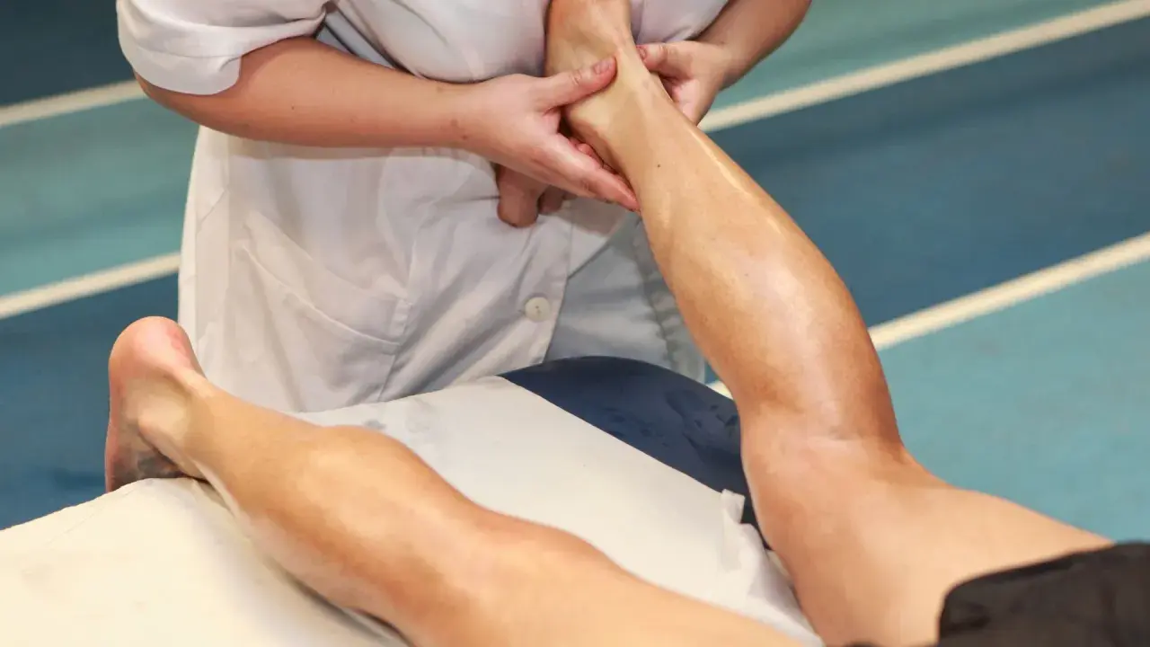 Mani esperte eseguono un massaggio trasverso profondo alla caviglia e al polpaccio di un atleta, alleviando la tensione muscolare.