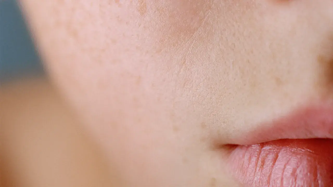 Primo piano di labbra e pelle raggrinzita, con leggere lentiggini e texture visibile.