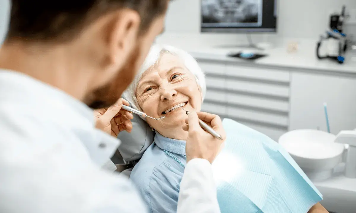 Un dentista esamina i denti di un'anziana sorridente, sottolineando l'importanza dell'igiene orale per gli anziani.