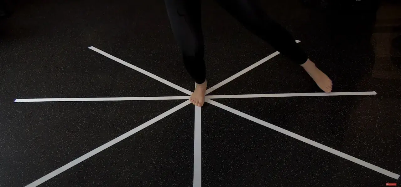 Persona esegue un test di equilibrio su un pavimento con nastro bianco a raggiera.
