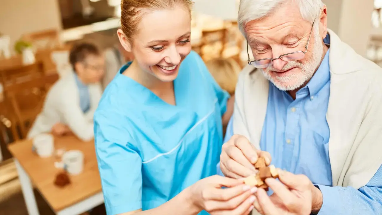 Assistente sorridente aiuta un anziano con demenza a completare un puzzle, mostrando come le fissazioni possano essere gestite con pazienza e attività stimolanti.