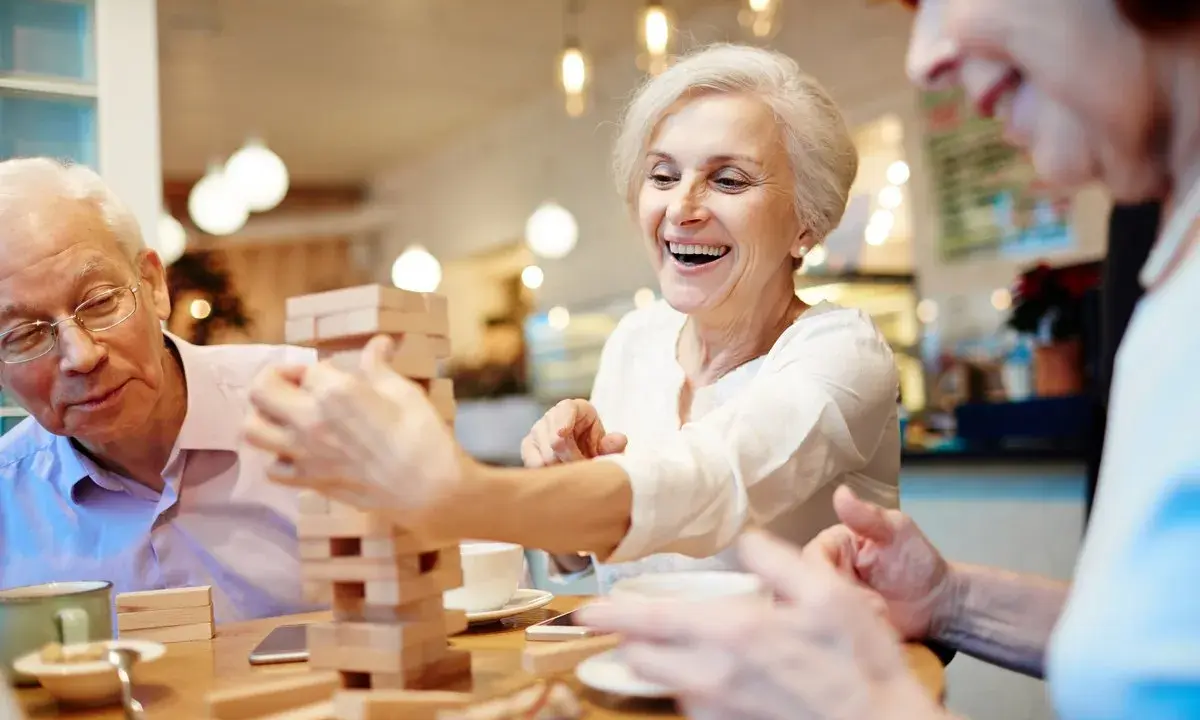 Anziani ridono giocando a Jenga, un esempio di iniziative per anziani che promuovono divertimento e socialità.
