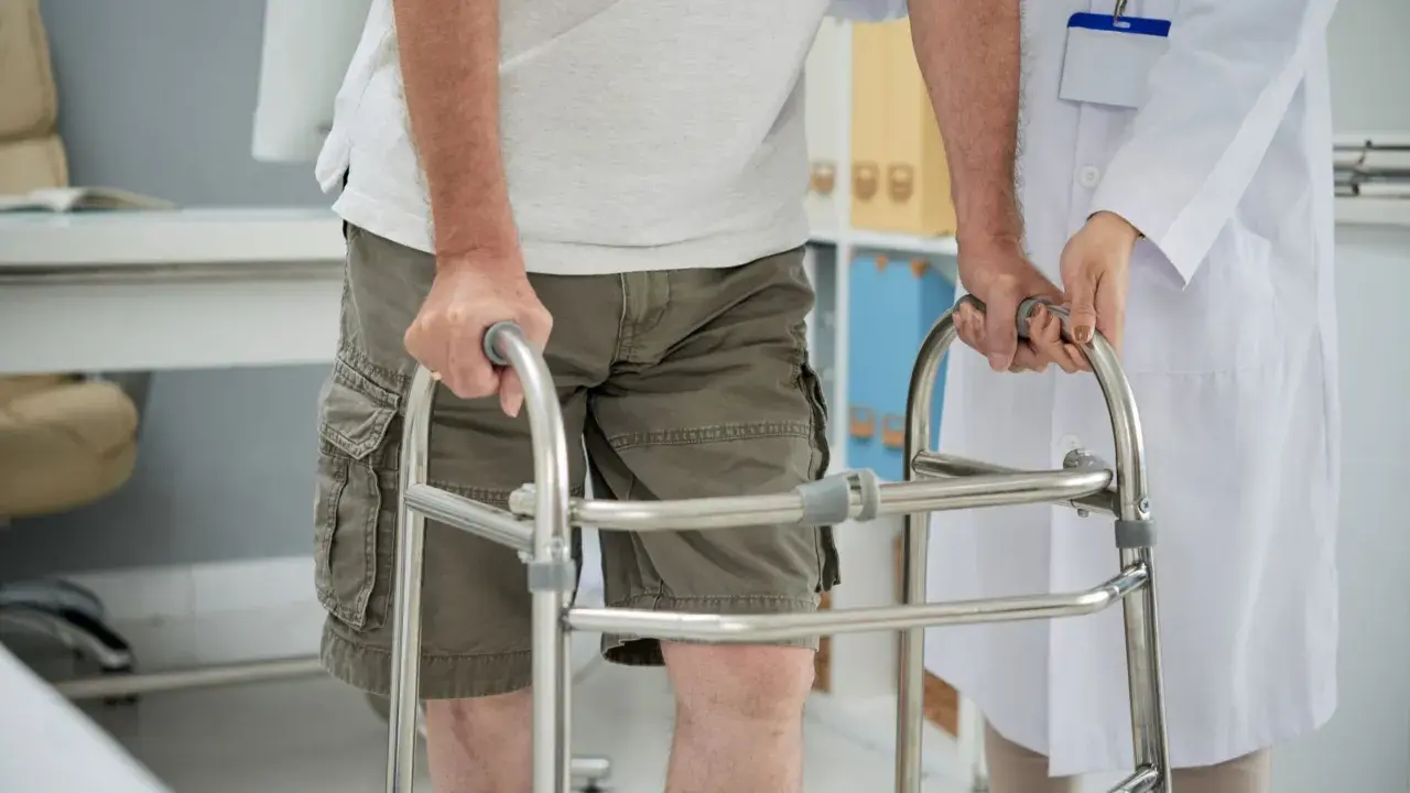 Paziente con problemi di deambulazione che si appoggia a un deambulatore, assistito da un medico.