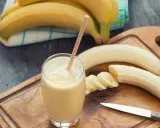 Frullato di banana in un bicchiere con una cannuccia, banane intere e affettate su un tagliere. Con la diarrea si può mangiare la banana, è un alimento delicato.