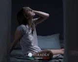 Donna sveglia di soprassalto nel letto, con la mano sulla fronte, soffre di sudorazione notturna. Cerca rimedi per dormire serenamente.