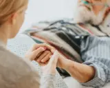 Mani che si stringono tra una giovane donna e un anziano in ospedale. Scopri cosa spetta a chi assiste un familiare con la 104.