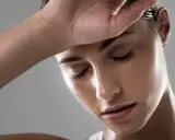 Donna con la mano sulla fronte, visibilmente stanca, con la pelle lucida per sudare tanto in testa e viso.