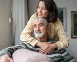 Un uomo anziano con Alzheimer, abbracciato da una donna, sembra cogliere un momento di lucidità, un ricordo che riaffiora.