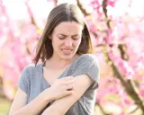 Donna con prurito in tutto il corpo la sera, graffiandosi il braccio tra i fiori rosa.