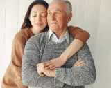 Un abbraccio affettuoso: un modo per come calmare una persona con demenza senile. La giovane donna stringe dolcemente l'anziano uomo, offrendo conforto e sicurezza.