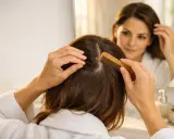Donna si pettina i capelli, cercando sollievo dal prurito al collo. Riflessa nello specchio, si tocca la testa con preoccupazione.