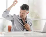 Uomo d'affari con camicia bagnata di sudore sotto le ascelle, che si sbottona la cravatta. Le cause del sudare freddo sono molteplici.