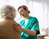 Infermiera sorridente incoraggia un'anziana con difficoltà a parlare, offrendo supporto e comprensione.