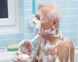 Un anziano con Alzheimer, coperto di schiuma, si lava. Un gesto di cura per convincerlo a lavarsi.