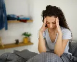 Donna con le mani sulle tempie, seduta a letto, soffre di giramenti di testa.
