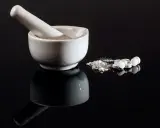 Mortaio e pestello con polvere bianca e pillole, forse per una preparazione farmaceutica con esenzione 013.