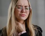 Donna con occhiali rossi si stringe la gola, visibilmente sofferente. Cerca rimedi per un prurito insopportabile.