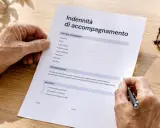 Mani anziane compilano un modulo per l'indennità di accompagnamento, chiedendosi dopo quanto tempo arriva l'assegno.