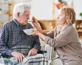 Una donna nutre con un cucchiaino il suo anziano nonno, che non mangia più, seduto su una sedia a rotelle.