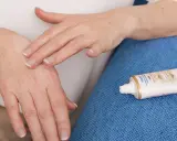 Mani che si massaggiano crema idratante per alleviare il prurito alle mani. Tubetto di Nivea Luminous 630 in primo piano.