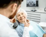 Un dentista esamina i denti di un'anziana sorridente, sottolineando l'importanza dell'igiene orale per gli anziani.