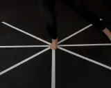 Persona esegue un test di equilibrio su un pavimento con nastro bianco a raggiera.