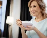 Donna sorride mentre mangia una zuppa cremosa, un esempio di cosa mangiare con disfagia.