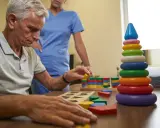 Esempi di terapia occupazionale anziani: un uomo anziano gioca con blocchi colorati, aiutato da un'infermiera.