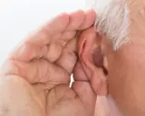 Mano di anziano che copre l'orecchio, forse per sentire meglio o per proteggersi da allucinazioni uditive.