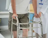 Paziente con problemi di deambulazione che si appoggia a un deambulatore, assistito da un medico.