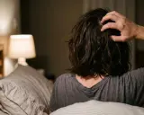 Persona a letto che si gratta la testa, forse perché il prurito aumenta di sera. Luce soffusa da una lampada.