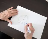 Mani anziane disegnano un orologio su carta, parte di un test memoria anziani.