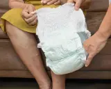 Mani che mostrano come si mette il pannolino a un'anziana seduta.