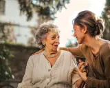 Una donna sorride alla madre anziana, con una mano sulla sua spalla. Finalmente posso portare mia mamma anziana a casa mia.