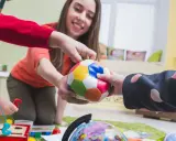 Bambini e terapista giocano con una palla colorata, un globo e un gioco di incastri. La terapia occupazionale cos'è? È questo: gioco e apprendimento.