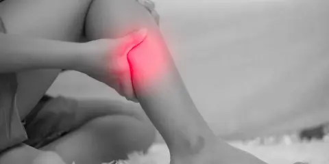 Donna che si tiene la gamba, evidenziata in rosso, a causa di dolori alle gambe, un possibile problema neurologico.
