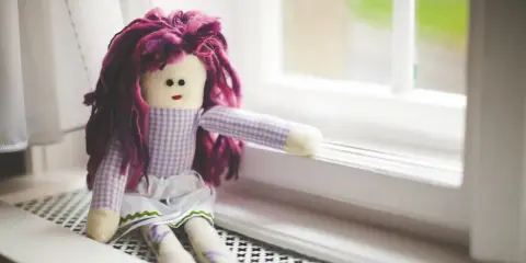Bambola con capelli viola, vestita a quadretti, seduta sul davanzale. Un simbolo di conforto nella doll therapy per l'Alzheimer.