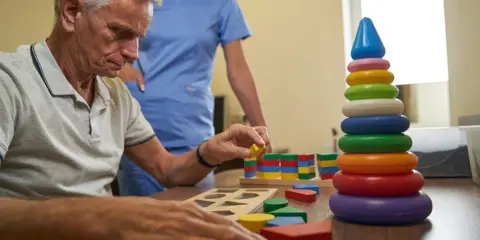 Esempi di terapia occupazionale anziani: un uomo anziano gioca con blocchi colorati, aiutato da un'infermiera.