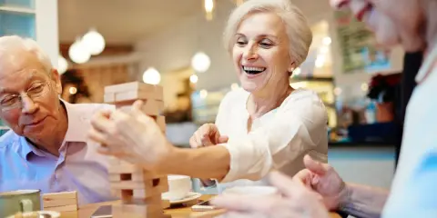 Anziani ridono giocando a Jenga, un esempio di iniziative per anziani che promuovono divertimento e socialità.